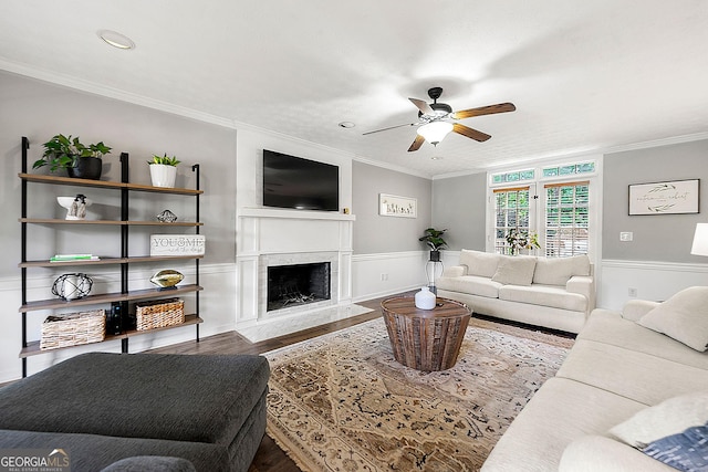 living room with ornamental molding, wainscoting, wood finished floors, a ceiling fan, and a premium fireplace