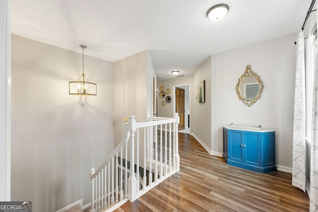 hall with baseboards, wood finished floors, and an upstairs landing