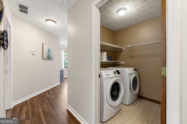 clothes washing area with a textured ceiling, laundry area, visible vents, and washer and clothes dryer