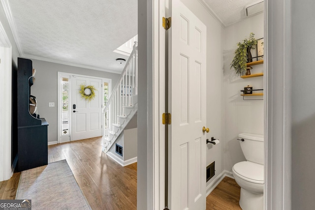 foyer entrance with crown molding, stairs, a textured ceiling, and wood finished floors