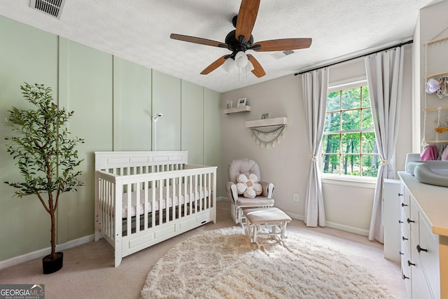bedroom with a nursery area, baseboards, light carpet, and a textured ceiling