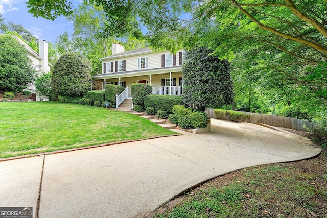 colonial-style house featuring a front yard, fence, covered porch, and a chimney