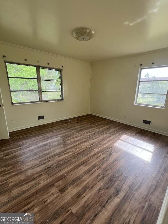 spare room featuring crown molding, dark wood-style flooring, baseboards, and visible vents