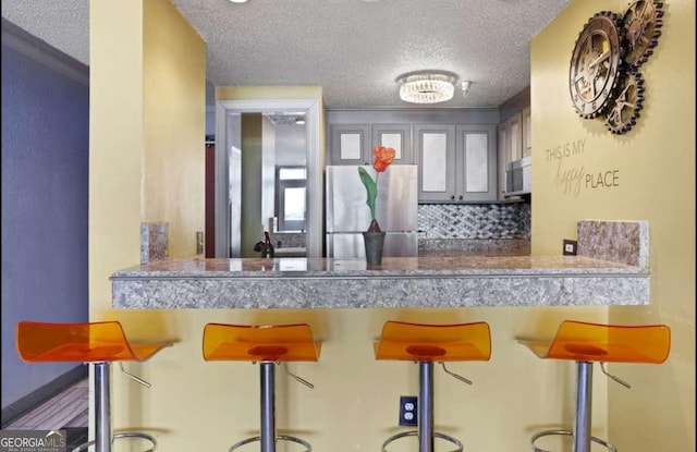 375 Ralph Mcgill Blvd # 1503, Atlanta, GA 30312 - kitchen with freestanding refrigerator, a textured ceiling, tasteful backsplash, and a kitchen breakfast bar