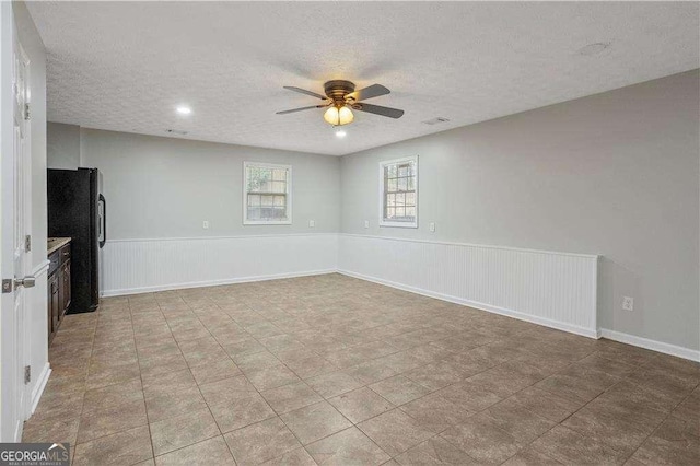 unfurnished living room featuring a ceiling fan, visible vents, a textured ceiling, and a wainscoted wall