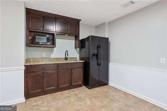 kitchen featuring a wainscoted wall, dark brown cabinets, visible vents, a sink, and black appliances