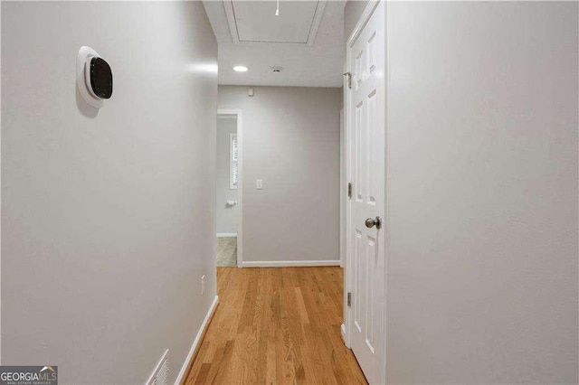 corridor featuring attic access, light wood-style floors, and baseboards