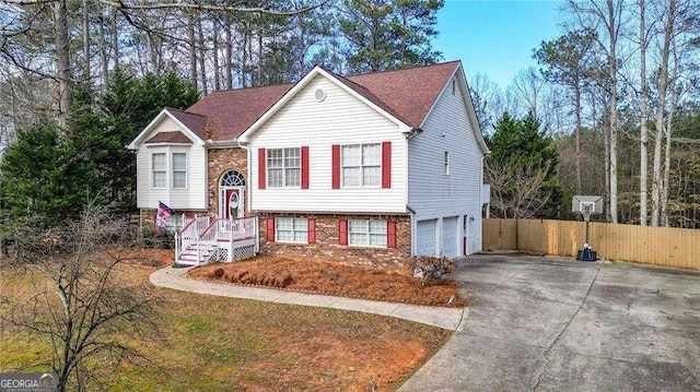 raised ranch with concrete driveway, an attached garage, fence, and brick siding