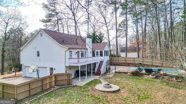 rear view of house with stairway, a chimney, a fenced backyard, a wooden deck, and a garage