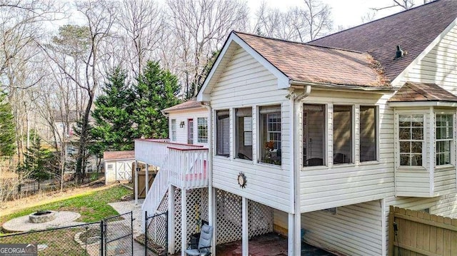 view of property exterior with a gate, an outdoor fire pit, a fenced backyard, roof with shingles, and a storage unit