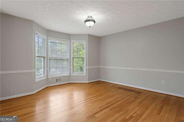 spare room with baseboards, a textured ceiling, and light wood finished floors