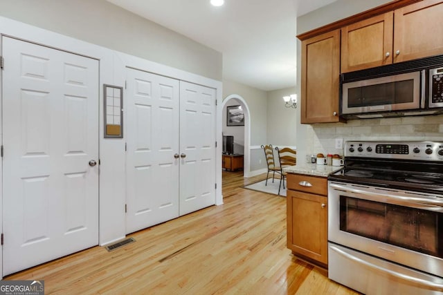 90 Hart Ave, Athens, GA 30606 - kitchen with stainless steel appliances, arched walkways, light wood finished floors, decorative backsplash, and brown cabinetry