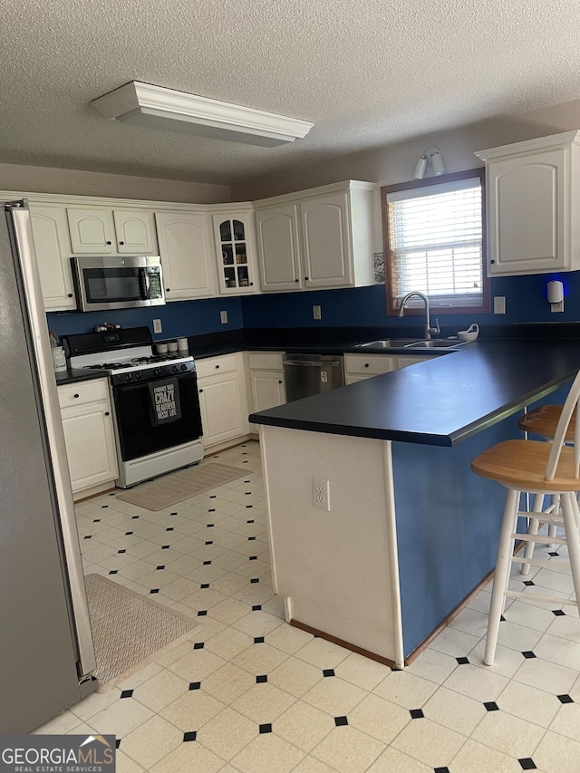 kitchen with a sink, stainless steel appliances, a breakfast bar, dark countertops, and a textured ceiling