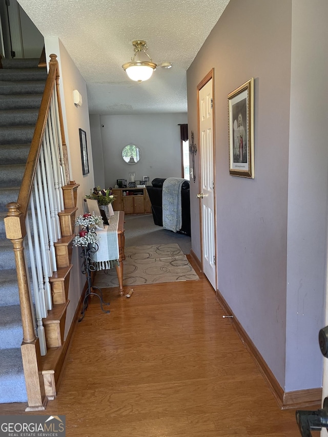corridor featuring a textured ceiling, light wood-style floors, baseboards, and stairs