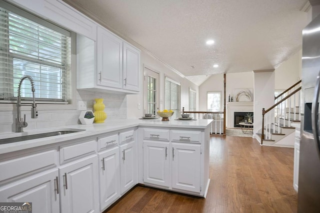 kitchen with white cabinets, a peninsula, a sink, a textured ceiling, and light countertops