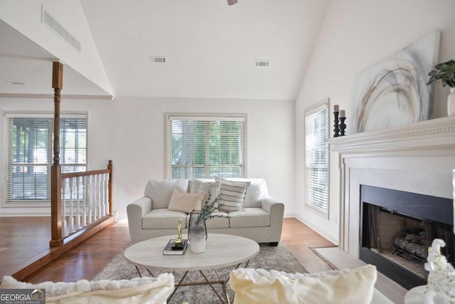 living room featuring a fireplace with flush hearth, vaulted ceiling, visible vents, and wood finished floors