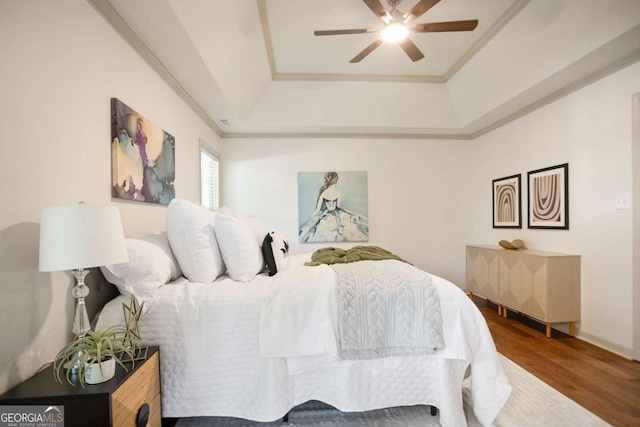bedroom featuring a ceiling fan, crown molding, wood finished floors, and a tray ceiling
