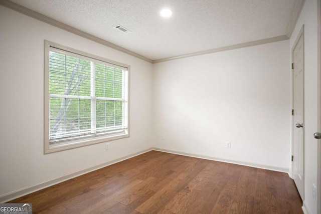 empty room featuring wood finished floors, a textured ceiling, baseboards, ornamental molding, and visible vents