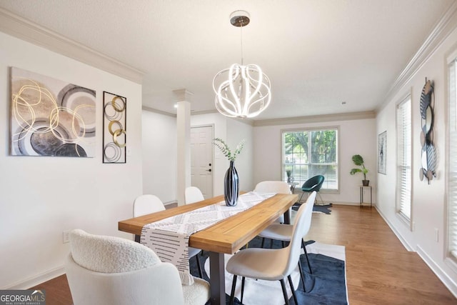 dining room featuring crown molding, wood finished floors, baseboards, a notable chandelier, and ornate columns