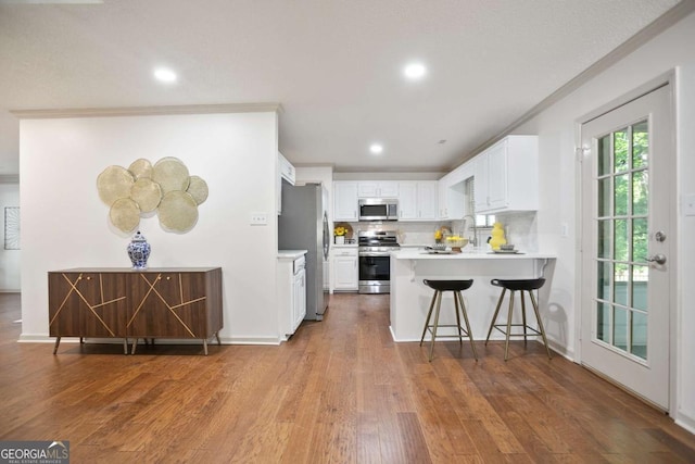 kitchen featuring stainless steel appliances, a peninsula, wood finished floors, and ornamental molding