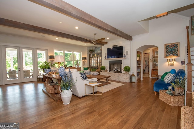 living area featuring beamed ceiling, wood finished floors, a ceiling fan, arched walkways, and french doors