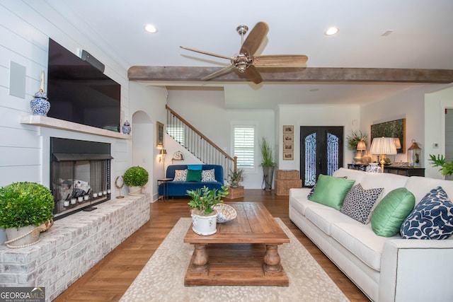 living area with beamed ceiling, recessed lighting, a brick fireplace, stairs, and wood finished floors
