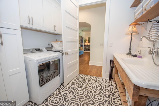 laundry room with cabinet space, independent washer and dryer, light wood-style flooring, baseboards, and arched walkways