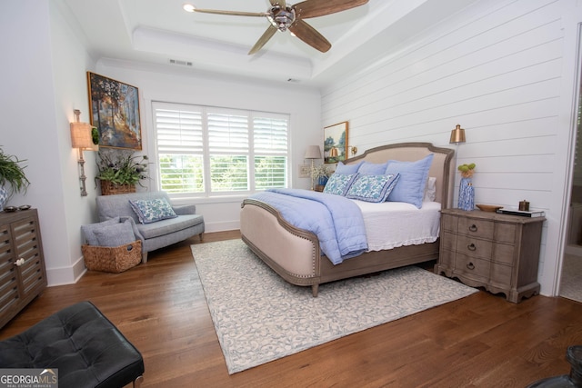 bedroom featuring a tray ceiling, a ceiling fan, visible vents, baseboards, and wood finished floors