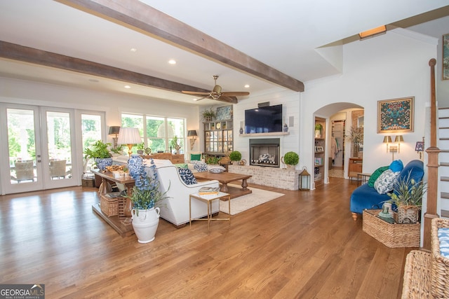 living area with beam ceiling, ceiling fan, wood finished floors, arched walkways, and french doors