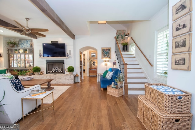 living area featuring arched walkways, wood finished floors, beamed ceiling, ceiling fan, and stairway