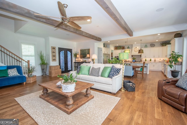 living area with beamed ceiling, a ceiling fan, stairway, and light wood-style floors