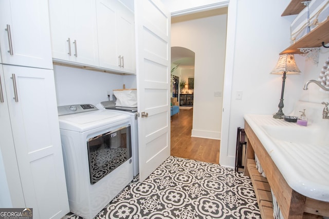 clothes washing area featuring light wood finished floors, a sink, cabinet space, washing machine and dryer, and arched walkways