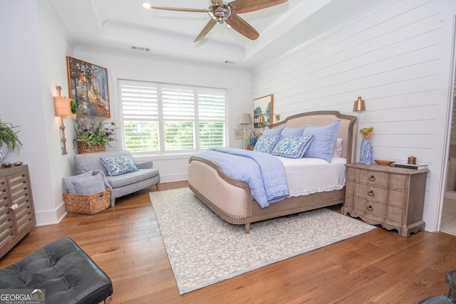 bedroom featuring wood finished floors, baseboards, visible vents, a ceiling fan, and a tray ceiling