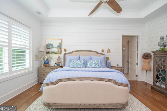 bedroom featuring wood finished floors, crown molding, visible vents, and a tray ceiling