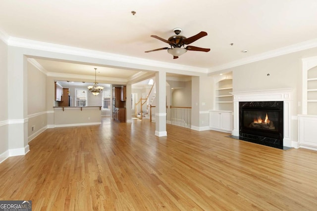 unfurnished living room featuring built in features, a fireplace, ceiling fan with notable chandelier, and ornamental molding