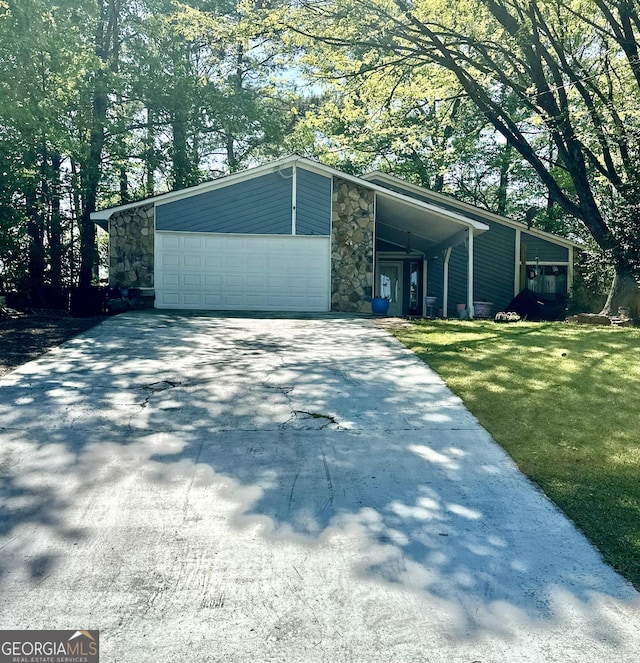 view of front of property featuring stone siding, driveway, a garage, and a front yard