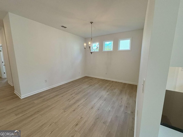 unfurnished dining area featuring an inviting chandelier, light wood-style floors, visible vents, and baseboards