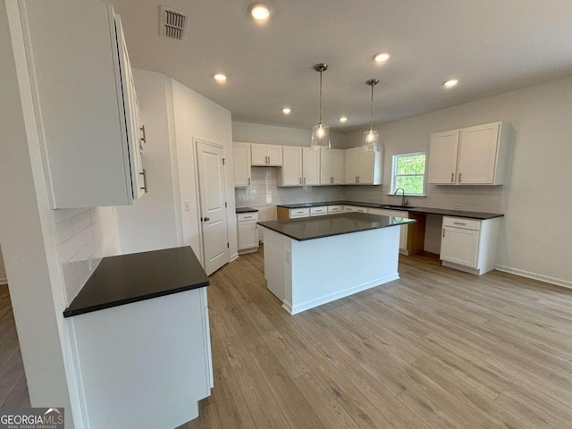 kitchen with light wood finished floors, visible vents, a sink, decorative backsplash, and white cabinetry