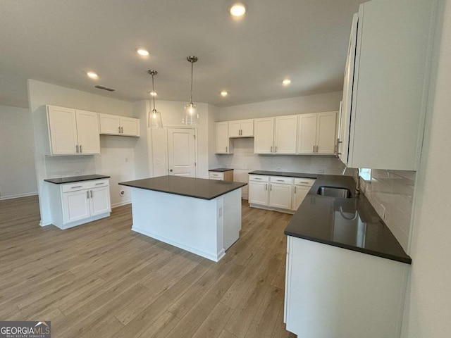 kitchen featuring decorative backsplash, dark countertops, a kitchen island, and light wood-type flooring