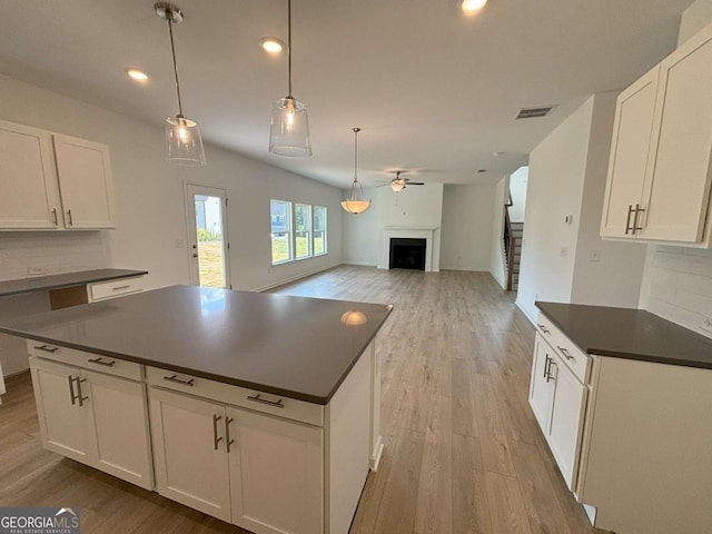 kitchen with light wood finished floors, tasteful backsplash, dark countertops, a ceiling fan, and a fireplace