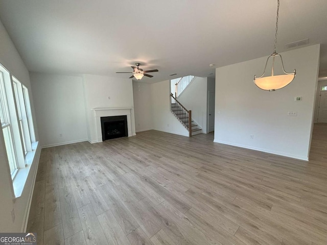 unfurnished living room featuring light wood-type flooring, a ceiling fan, a fireplace, and stairway
