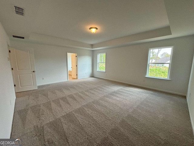 carpeted empty room with baseboards, a tray ceiling, and visible vents