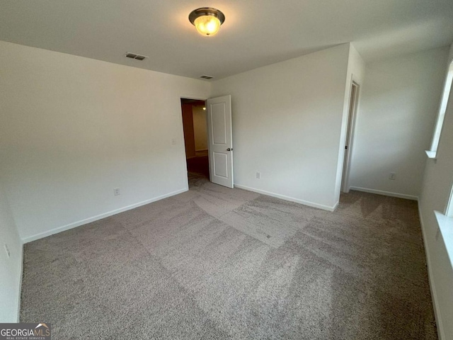 unfurnished room with carpet, visible vents, and baseboards