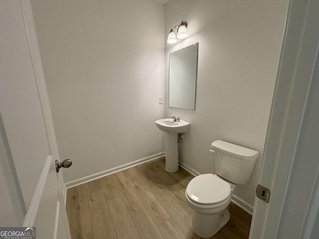 bathroom featuring wood finished floors, toilet, baseboards, and a sink