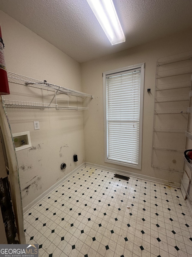 clothes washing area with a textured ceiling, hookup for a washing machine, baseboards, tile patterned floors, and electric dryer hookup
