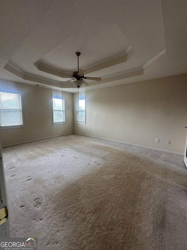 unfurnished room with a tray ceiling, ornamental molding, carpet floors, ceiling fan, and baseboards