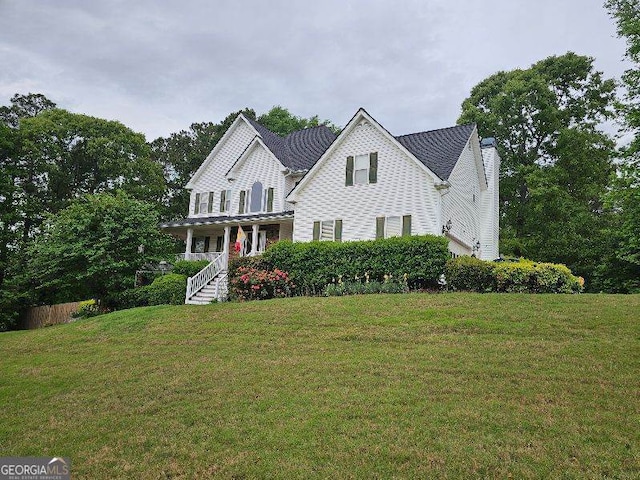 view of front facade featuring a front yard, covered porch, and a chimney
