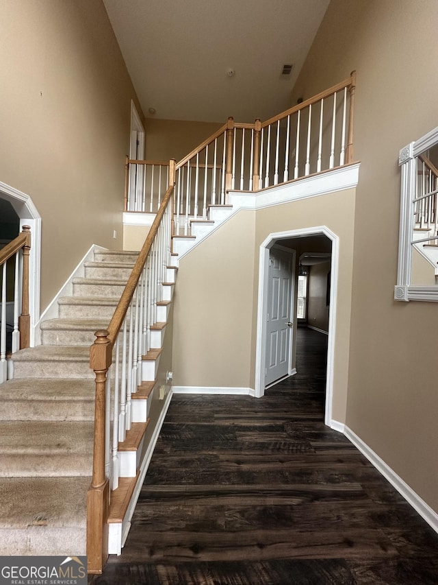 stairway with wood finished floors, baseboards, arched walkways, and a towering ceiling