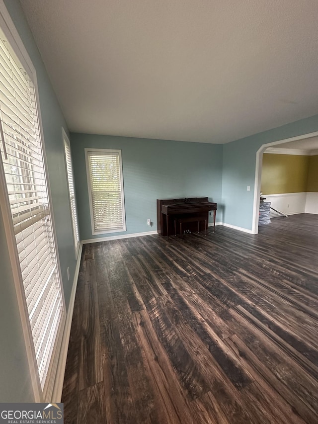unfurnished living room with wood finished floors, baseboards, and arched walkways