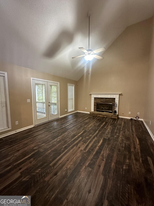 unfurnished living room featuring dark wood-type flooring, ceiling fan, vaulted ceiling, a fireplace, and french doors